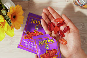 Hand holding Annie's fruit snacks in palm with Annie's purple packing below